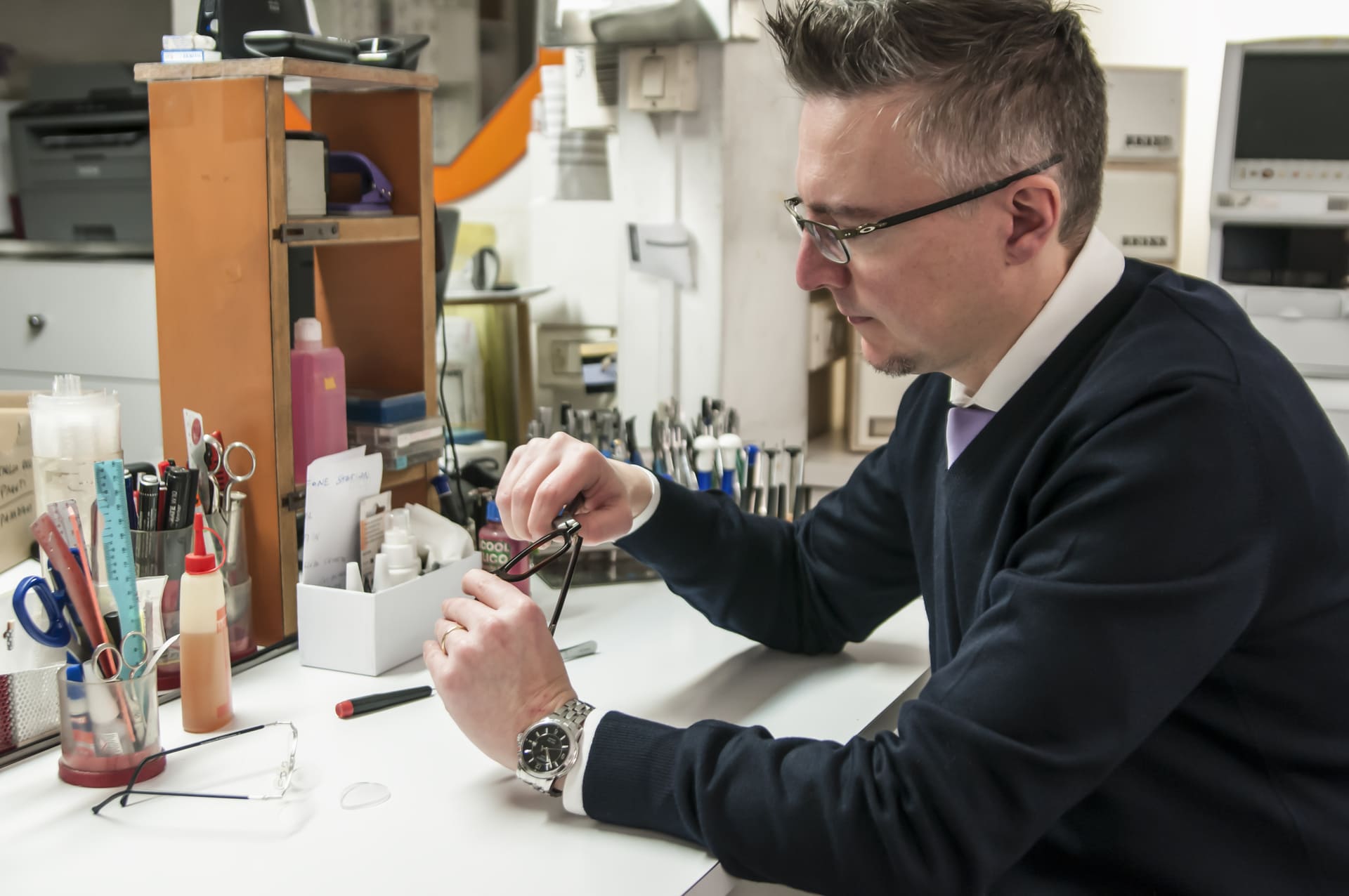 Un uomo con occhiali da vista e maglione è seduto mentre ripara occhiali - Crisafulli Eyewear a Milano