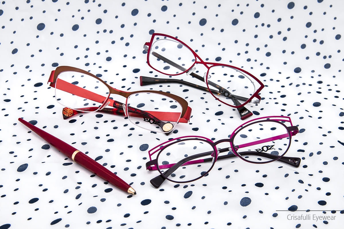 Una collezione di tre paia di occhiali da vista eleganti su uno sfondo a pois blu - Crisafulli Eyewear a Milano