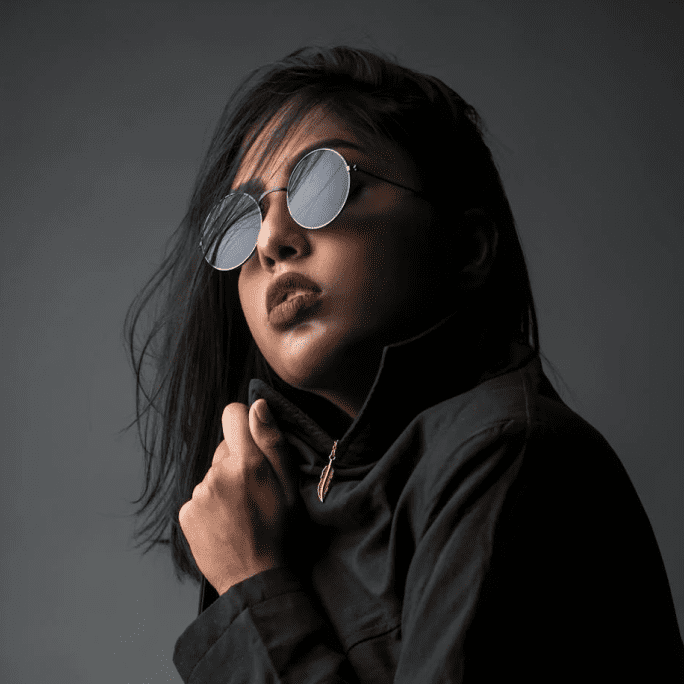 Una donna che indossa occhiali da sole e una giacca scura posa su uno sfondo grigio. - Crisafulli Eyewear a Milano
