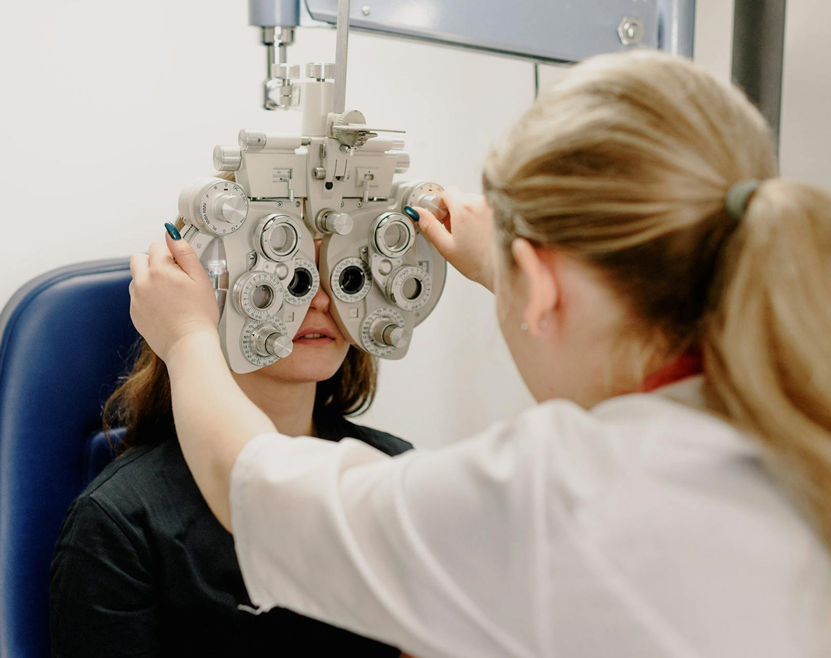An ophthalmologist adjusts a phoropter in front of a patient sitting in a blue chair - Crisafulli Eyewear in Milan